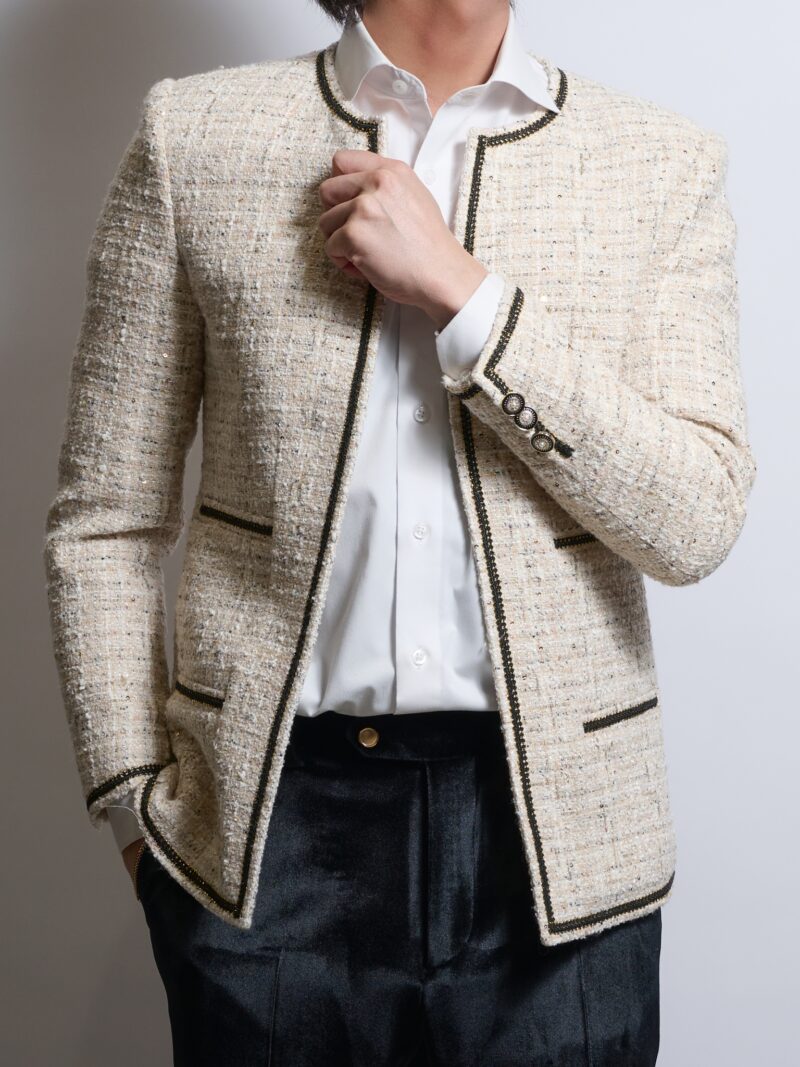 ブレークツイードアイボリーノーカラージャケットを着る男性